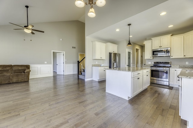 kitchen with light stone counters, a kitchen island, wood finished floors, open floor plan, and appliances with stainless steel finishes