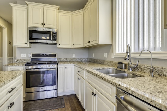 kitchen featuring light stone counters, dark wood finished floors, a sink, stainless steel appliances, and white cabinetry