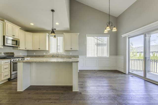 kitchen with a kitchen island, dark wood finished floors, wainscoting, stainless steel appliances, and a sink