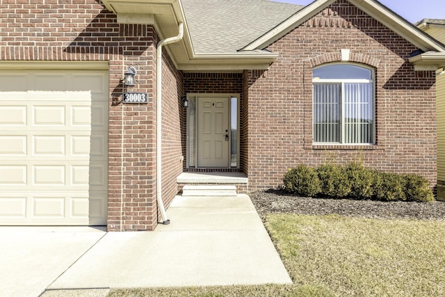 doorway to property with brick siding, a garage, and a shingled roof