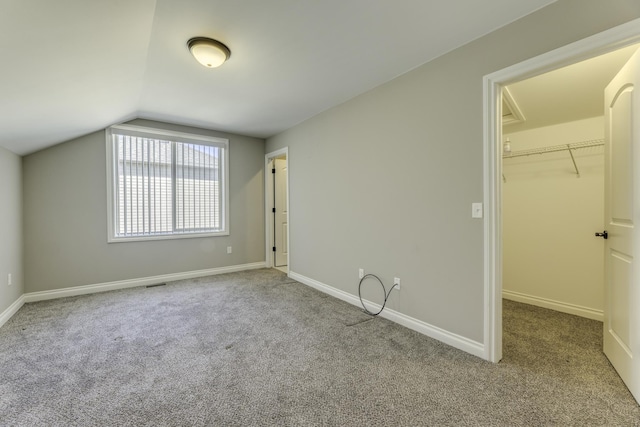 unfurnished bedroom with carpet flooring, baseboards, a walk in closet, and lofted ceiling