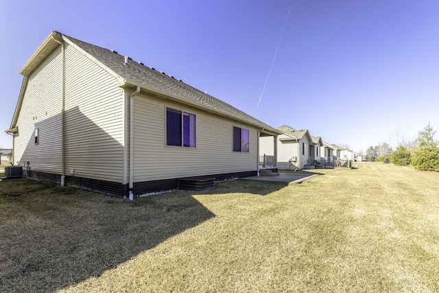 view of side of home with a yard, central AC unit, a patio, and roof with shingles