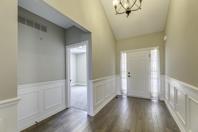 foyer featuring visible vents, a wainscoted wall, dark wood-type flooring, an inviting chandelier, and a decorative wall