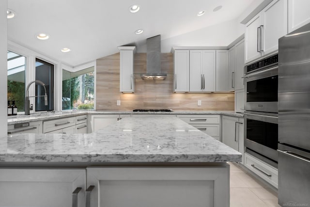 kitchen with light stone counters, tasteful backsplash, appliances with stainless steel finishes, wall chimney range hood, and vaulted ceiling