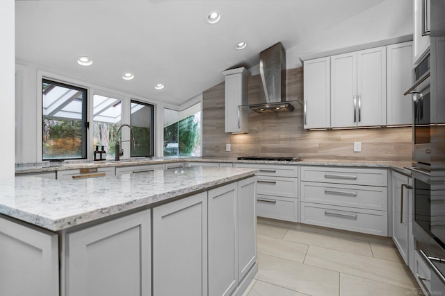 kitchen featuring a sink, tasteful backsplash, wall chimney exhaust hood, light tile patterned floors, and vaulted ceiling