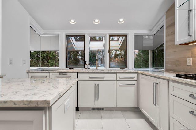 kitchen with a skylight, light tile patterned floors, recessed lighting, and light stone counters