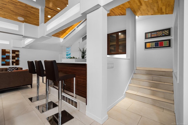 bar featuring light tile patterned flooring, baseboards, wood ceiling, stairs, and vaulted ceiling