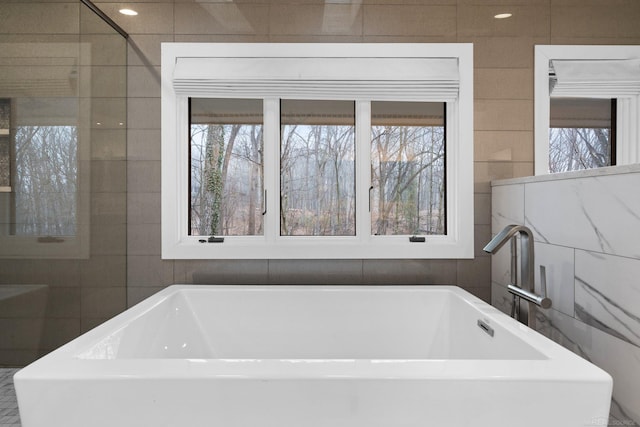 bathroom with tile walls, a soaking tub, and plenty of natural light