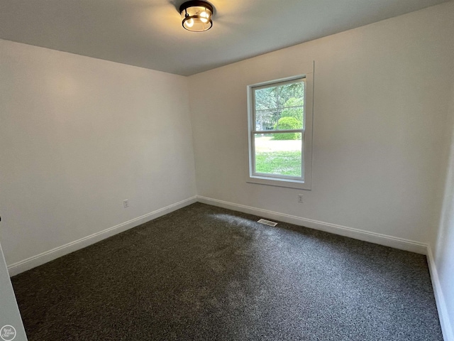 empty room with dark colored carpet, visible vents, and baseboards