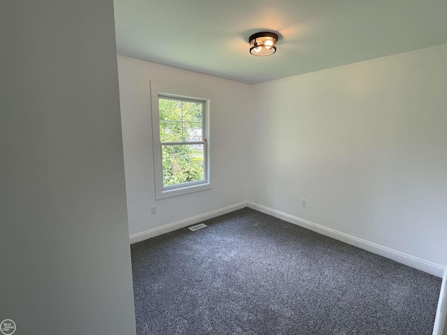 unfurnished room featuring baseboards, visible vents, and dark carpet