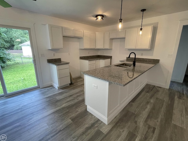 kitchen with a sink, a peninsula, dark wood finished floors, and dark stone countertops