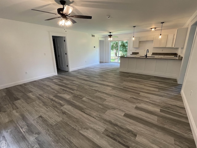 unfurnished living room featuring ceiling fan, dark wood-type flooring, baseboards, and a sink