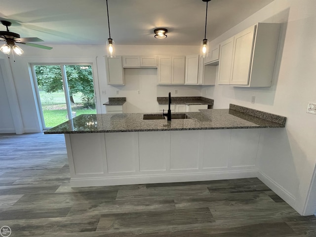 kitchen with dark wood-style floors, a peninsula, dark stone counters, and a sink