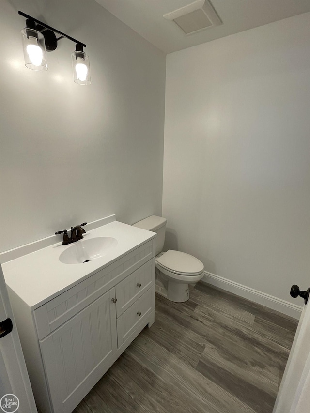 bathroom with vanity, toilet, wood finished floors, and baseboards