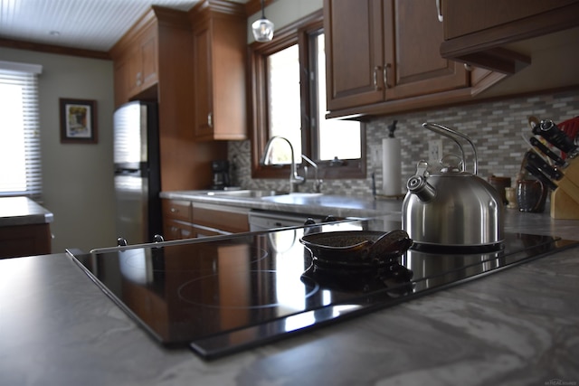 kitchen with a sink, tasteful backsplash, brown cabinetry, and freestanding refrigerator