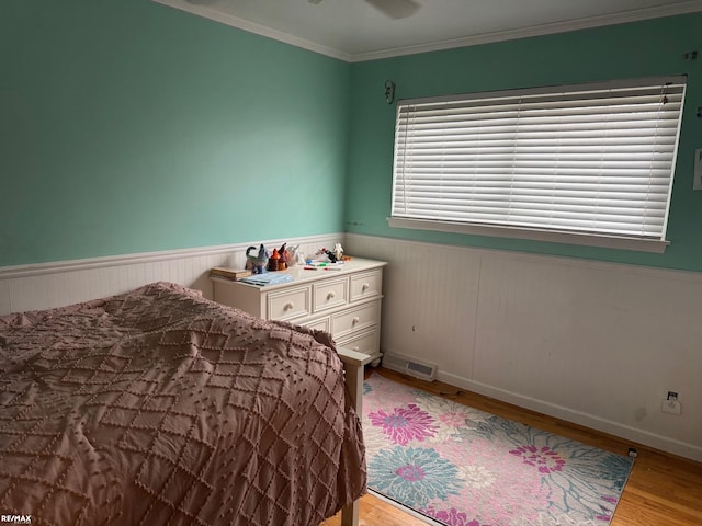 bedroom with light wood finished floors, visible vents, crown molding, and a wainscoted wall