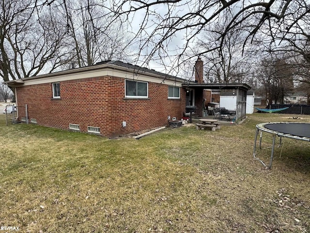 exterior space featuring a trampoline, a lawn, brick siding, and a chimney