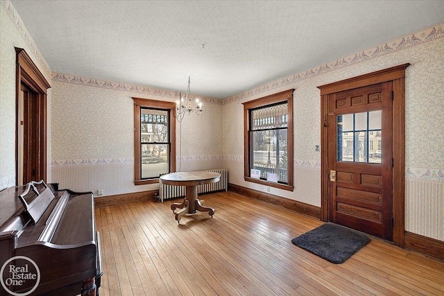 entryway featuring wallpapered walls, radiator heating unit, an inviting chandelier, and wood-type flooring