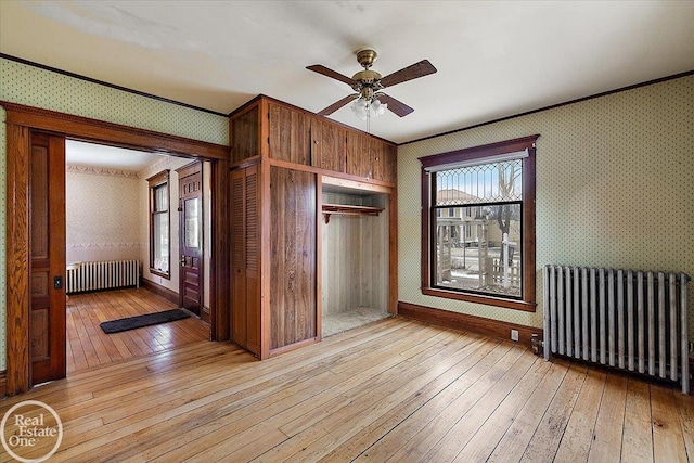 interior space featuring wallpapered walls, radiator, baseboards, and light wood-type flooring