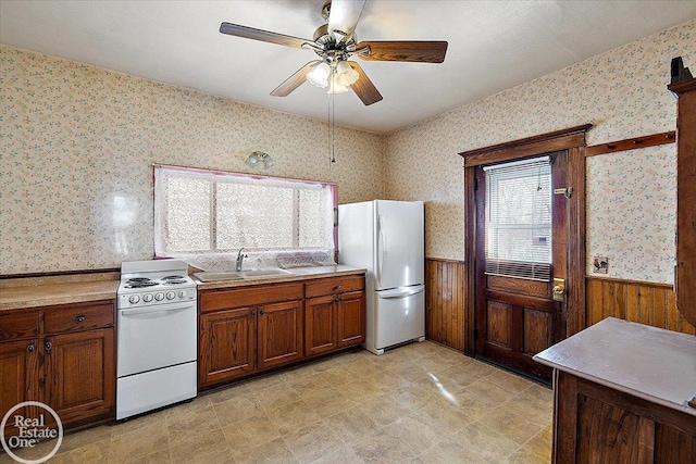 kitchen with a wainscoted wall, a sink, wallpapered walls, white appliances, and light countertops