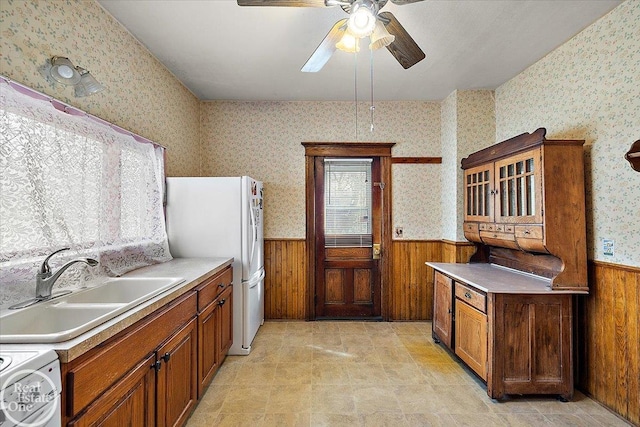 kitchen featuring a sink, brown cabinets, wainscoting, and wallpapered walls