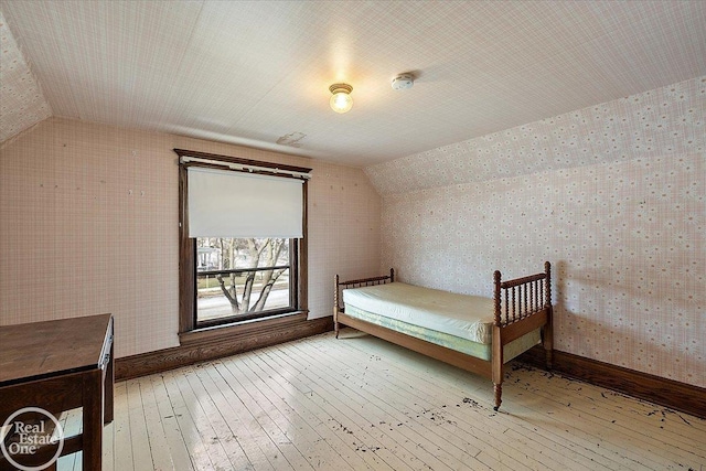 unfurnished bedroom with lofted ceiling, baseboards, and light wood finished floors