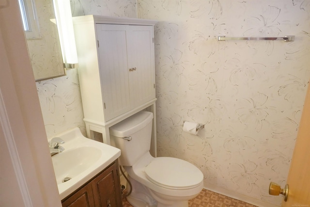 half bath featuring tile patterned floors, toilet, vanity, and wallpapered walls