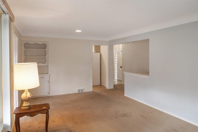 spare room featuring light carpet, visible vents, and baseboards