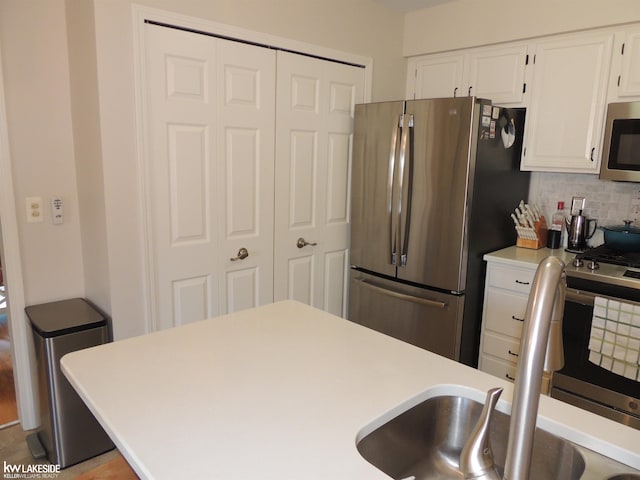 kitchen featuring backsplash, light countertops, stainless steel appliances, white cabinetry, and a sink