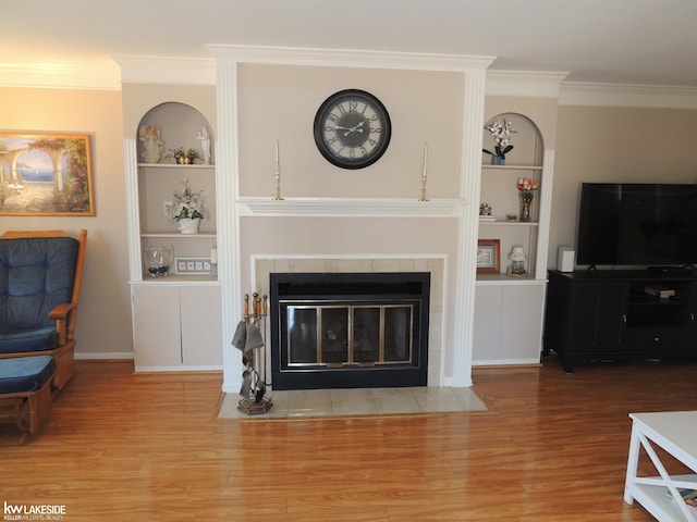 living room with built in features, a fireplace, crown molding, and wood finished floors