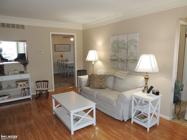 living room with a ceiling fan, wood finished floors, visible vents, baseboards, and crown molding