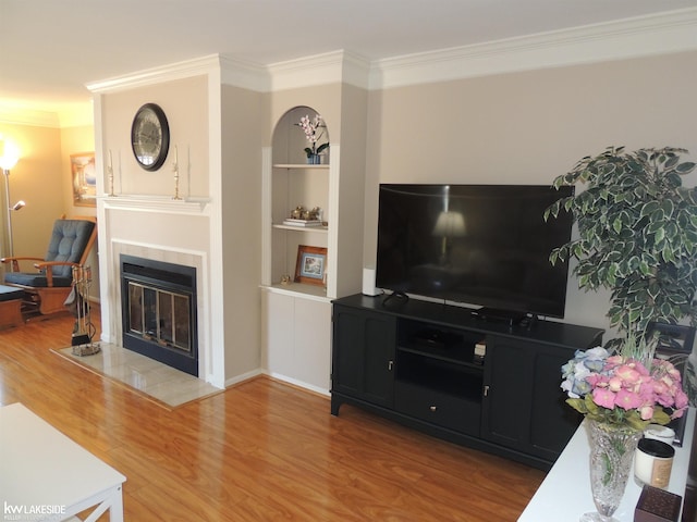 living room featuring a fireplace, crown molding, built in shelves, and wood finished floors