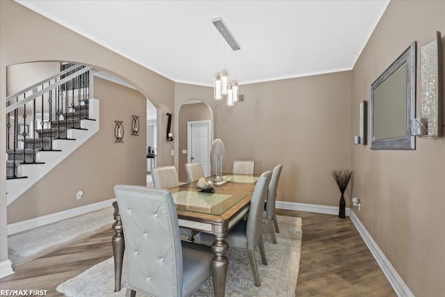 dining space with crown molding, baseboards, stairway, wood finished floors, and arched walkways