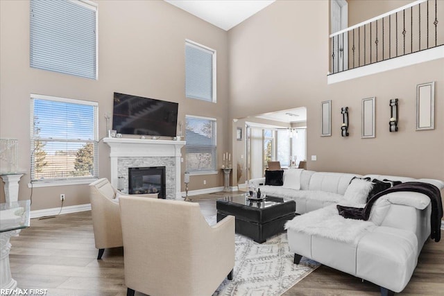 living room featuring a stone fireplace, a high ceiling, wood finished floors, and baseboards