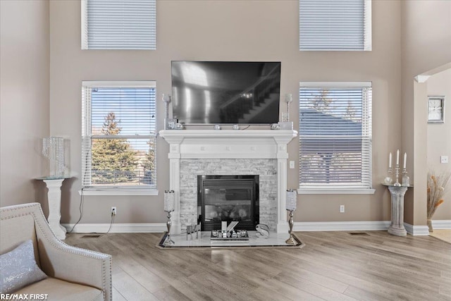 living area with visible vents, baseboards, a stone fireplace, and wood finished floors