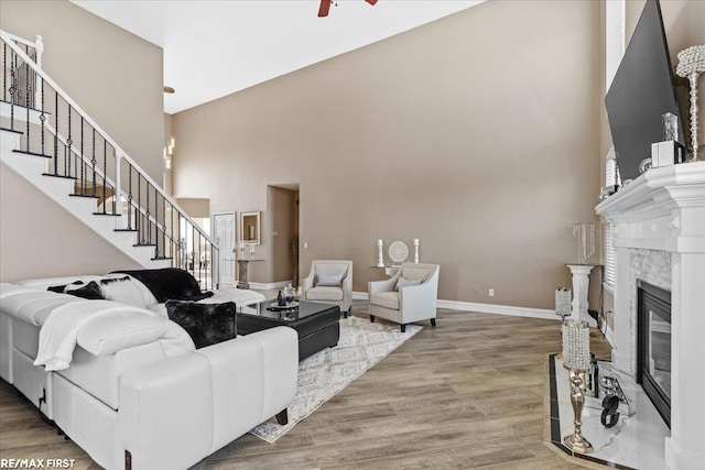 living room featuring baseboards, stairs, a premium fireplace, a high ceiling, and wood finished floors