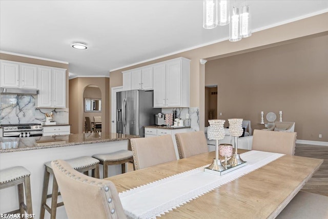 dining area with crown molding, wood finished floors, arched walkways, and baseboards