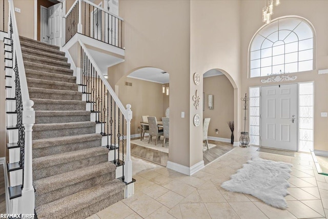 foyer entrance featuring tile patterned flooring, visible vents, baseboards, a towering ceiling, and arched walkways