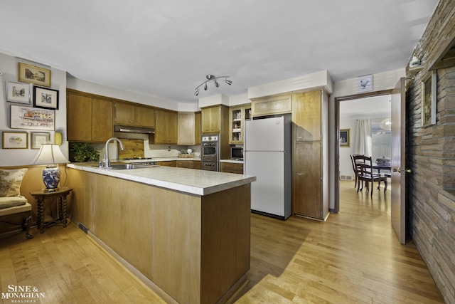 kitchen featuring a sink, light wood-style floors, appliances with stainless steel finishes, a peninsula, and light countertops