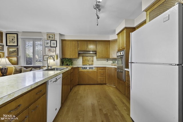 kitchen with under cabinet range hood, light countertops, brown cabinets, white appliances, and a sink