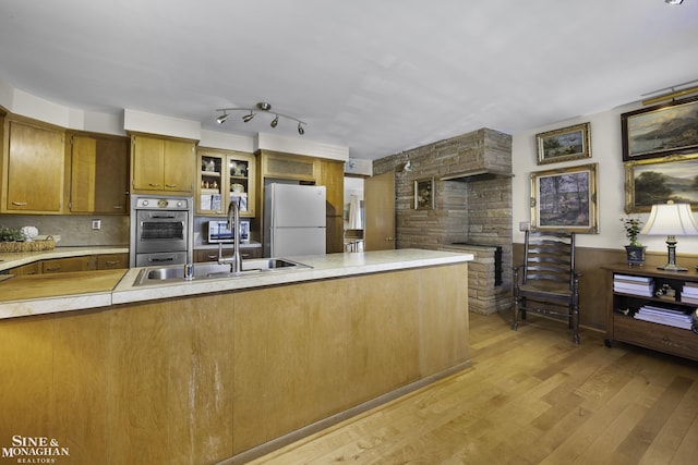 kitchen featuring brown cabinets, freestanding refrigerator, oven, light countertops, and light wood-type flooring