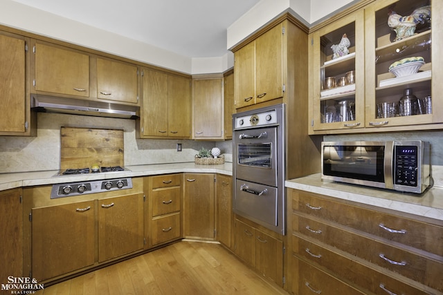 kitchen featuring light wood-style flooring, light countertops, under cabinet range hood, appliances with stainless steel finishes, and a warming drawer