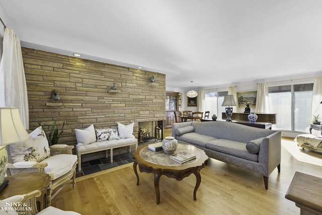 living area with light wood finished floors, a stone fireplace, and a healthy amount of sunlight