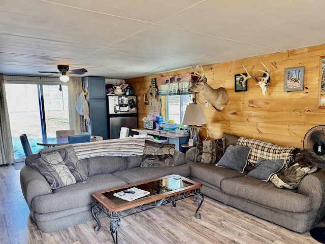 living room with a ceiling fan, wooden walls, and wood finished floors