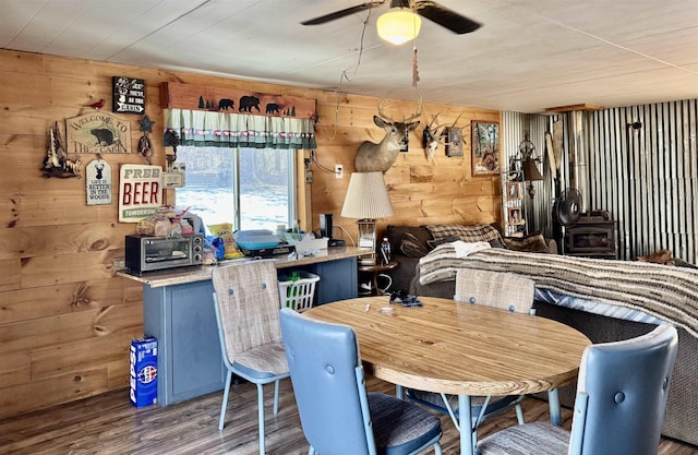 dining area featuring a ceiling fan, wood finished floors, wooden walls, a toaster, and a wood stove