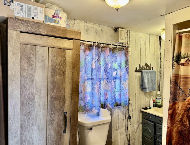 bathroom featuring toilet, wood walls, and vanity