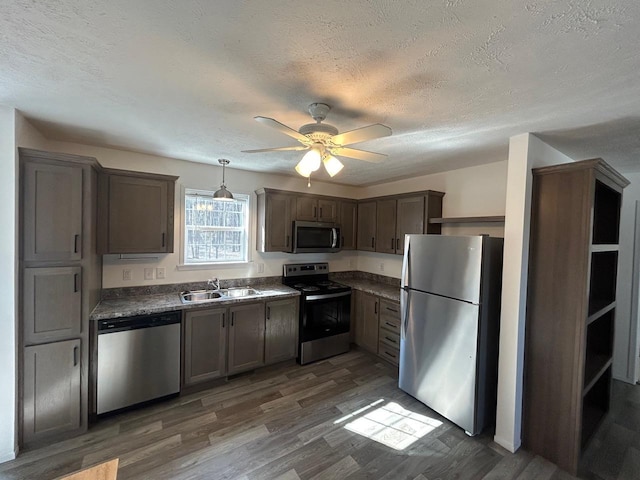 kitchen featuring wood finished floors, a sink, ceiling fan, stainless steel appliances, and dark countertops