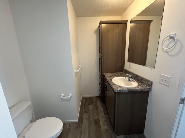 bathroom featuring baseboards, toilet, vanity, wood finished floors, and a textured ceiling