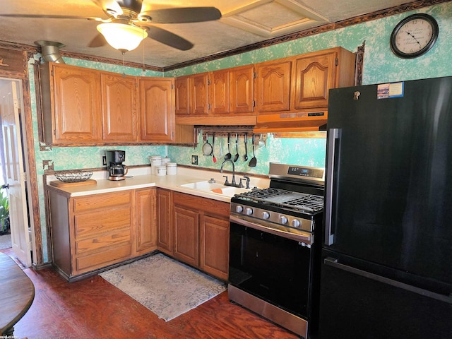 kitchen featuring under cabinet range hood, black refrigerator, wallpapered walls, light countertops, and stainless steel gas range