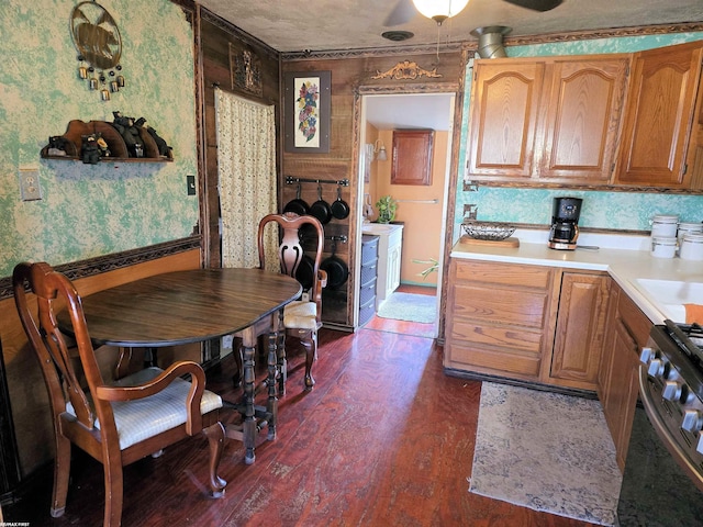 kitchen featuring brown cabinetry, wallpapered walls, light countertops, dark wood-type flooring, and stainless steel gas range oven